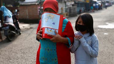 A woman wearing a drawing book as a mask and a girl wearing a protective mask walk amid the coronavirus disease (COVID-19) outbreak, in Depok near Jakarta, Indonesia, April 13, 2020. REUTERS