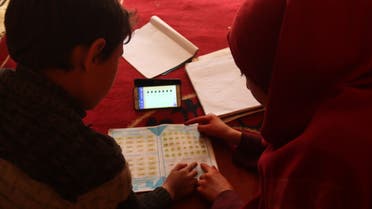 Um Yazan’s children study their lessons in the family’s tent, sharing a single mobile phone to follow along with the teacher on April 5. (Muhammad Al Hosse)