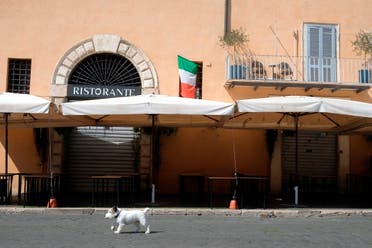 A dog passes by a closed restaurant as an Italian flag hangs from a window, in Rome on April 7, 2020. (AP)