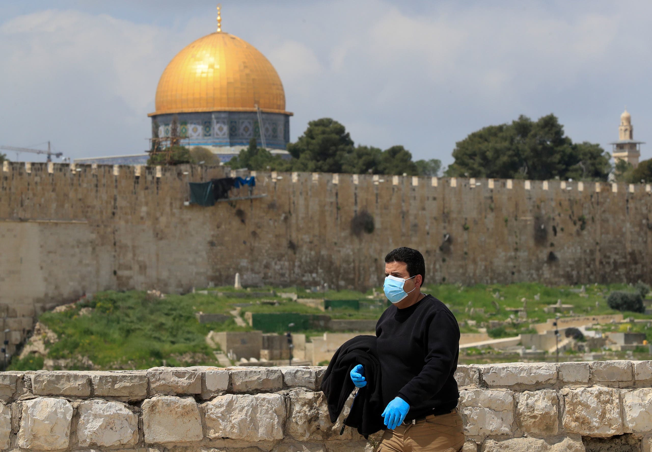 A man wearing a mask and gloves walks past the Dome of the Rock mosqu in Jerusalem's Old City on April 2, 2020. (AFP)