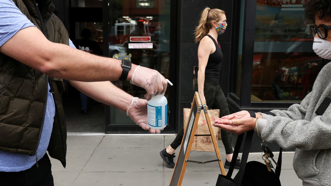 A store worker offers hand sanitizer to shoppers, during the coronavirus disease (COVID-19) outbreak, as they wait in line on the sidewalk outside a grocery store in Washington, U.S., April 14, 2020. REUTERS/Jonathan Ernst
