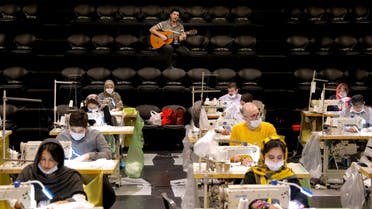 Volunteers wearing face masks to curb the spread of the new coronavirus, sew face masks, as a guitarist plays for volunteers, at the Hafez theatre hall in downtown Tehran, Iran, Wednesday, April 15, 2020. (AP