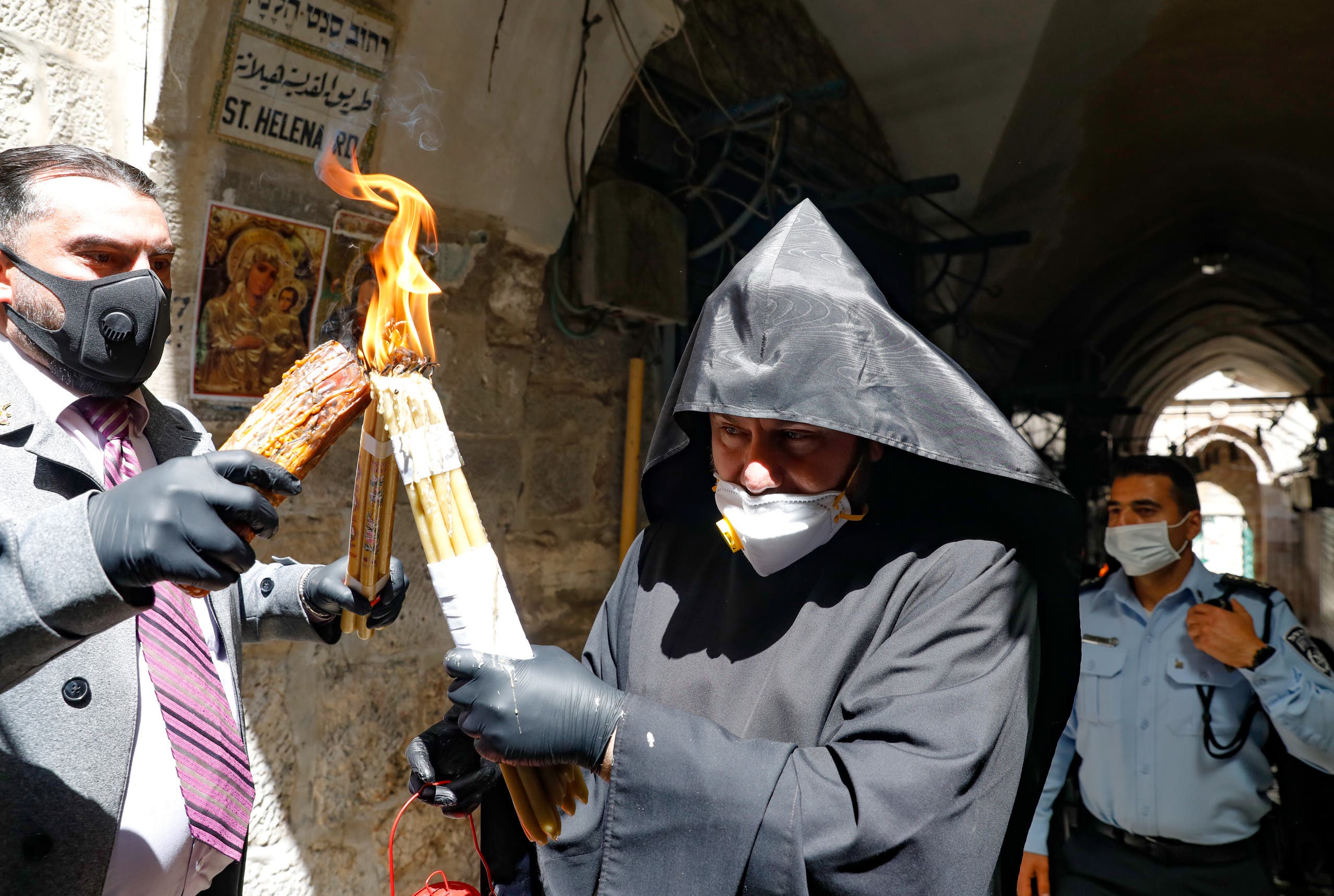 An Armenian priest wearing a protective mask and gloves passes on the Holy Fire lit in the church of the Holy Sepulchre, as very few Orthodox Christians gather in Jerusalem's Old City to celebrate Easter due to the lockdown imposed by authorities in a bid to limit the spread of the novel coronavirus, on April 18, 2020. (AFP)