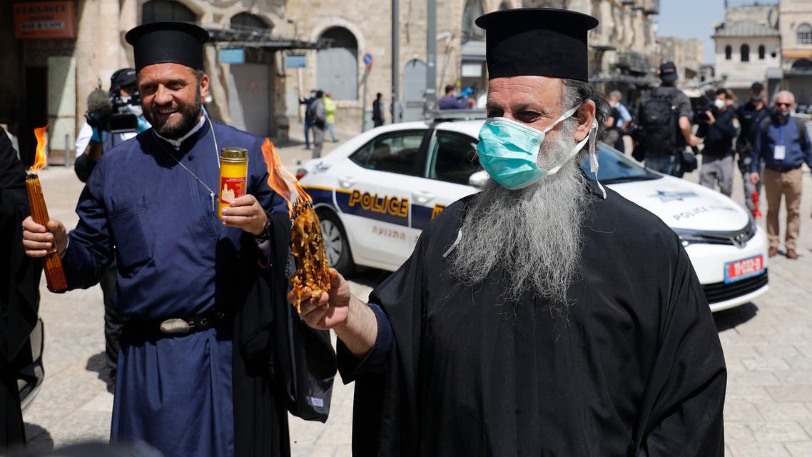 Greek Orthodox priests hold candles lit from the Holy Fire in the church of the Holy Sepulchre, as very few Orthodox Christians gather in Jerusalem's Old City to celebrate Easter due to the lockdown imposed by authorities in a bid to limit the spread of the novel coronavirus, on April 18, 2020. (AFP)