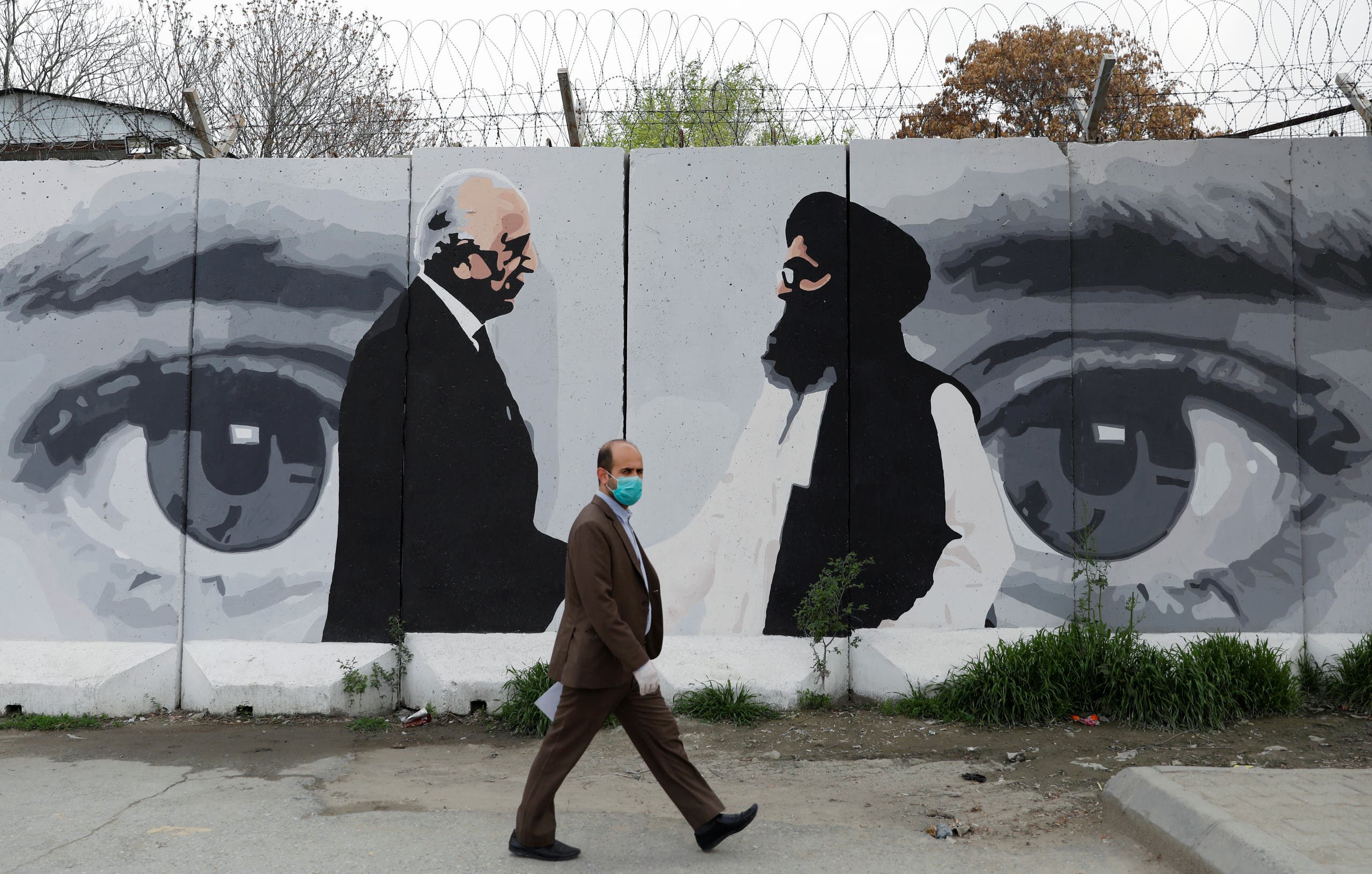 An Afghan man wearing a protective face mask walks past a wall painted with photo of Zalmay Khalilzad, US envoy for peace in Afghanistan, and Mullah Abdul Ghani Baradar, the leader of the Taliban delegation, in Kabul, Afghanistan on April 13, 2020. (Reuters)