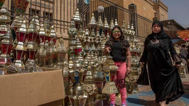 A girl poses for a photograph with a lantern she just bought with her mother as a woman makes her way through a market, in the Sayeda Zeinab neighborhood of Cairo, Egypt, Tuesday, April 21, 2020.  (AP)