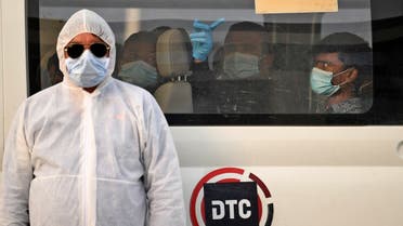 A health worker stands in front of a bus driving migrant workers who have been tested positive for the COVID-19 to the Warsan neighbourhood, where people infected or suspected of being infected by the virus are quarantined, in the Gulf Emirate of Dubai. (AFP)