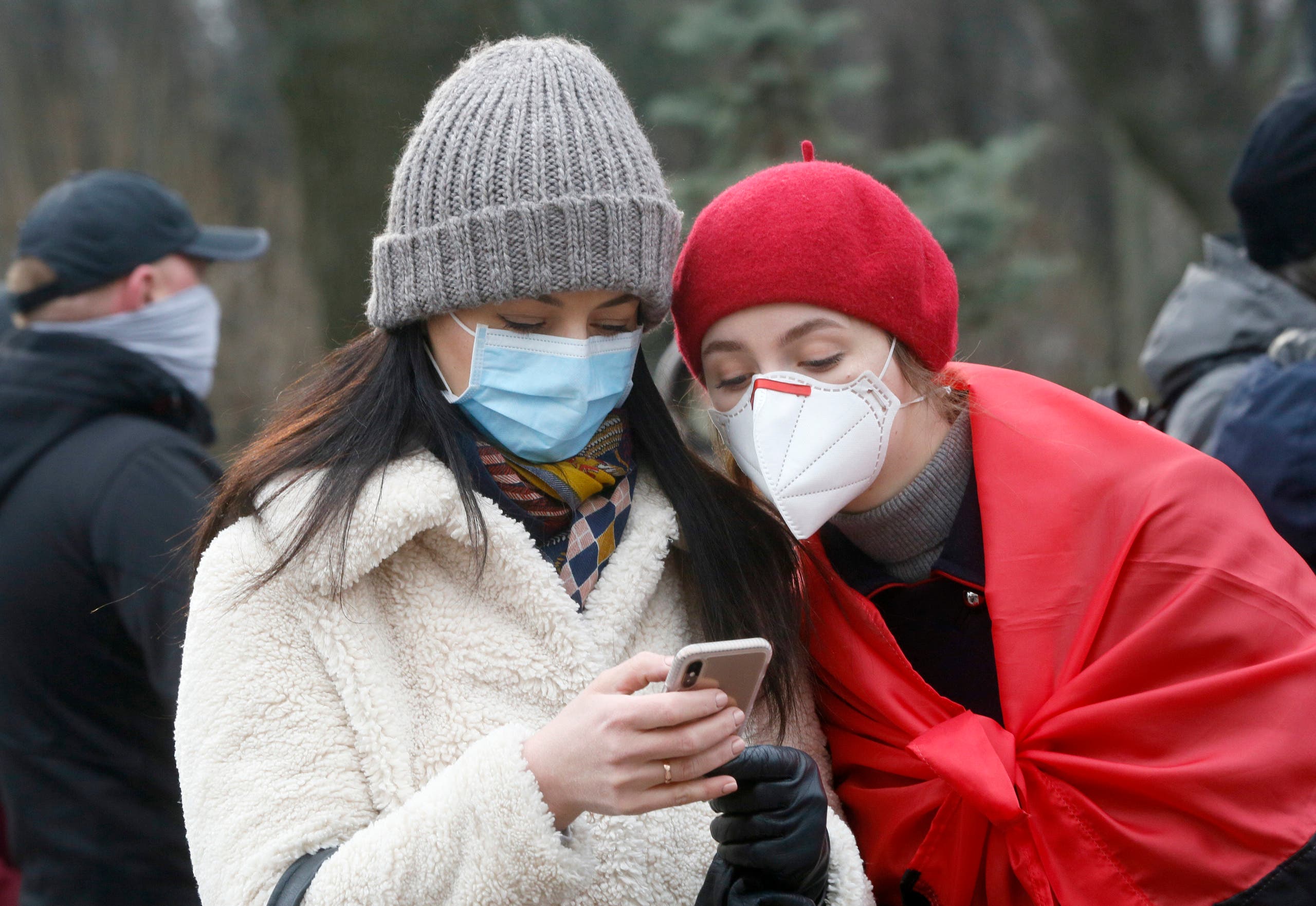 Two women wearing face masks look at the latest news on a phone. (File photo: AP)