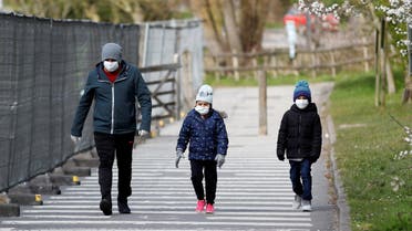 A man and children wearing protective face masks walk near a Chessington World of Adventures car park, which has been turned into a testing facility as the spread of the coronavirus disease (COVID-19) continues, Chessington, Britain. (Reuters)