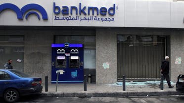 Men walk near broken glass from a damaged Bankmed branch in Tripoli, Lebanon November 27, 2019. (Reuters)