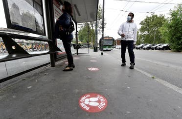People wearing protective face masks wait for a bus at the stop with social distancing signs on the pavement as the spread of the coronavirus continues, in Milan, Italy, on April 27, 2020. (Reuters)