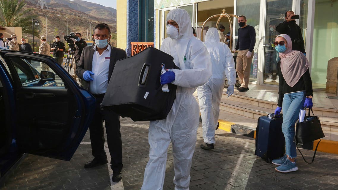 A worker helps a mask-clad woman with her baggage as she prepares to leave a Dead Sea resort where she has been quarantined for 14 days, approximately 60 kilometres sout of the Jordanian capital Amman on March 30, 2020. Jordanian authorities started to take home about 5,000 people quarantined in hotels to guard against the spread of coronavirus since their return to the country two weeks ago.