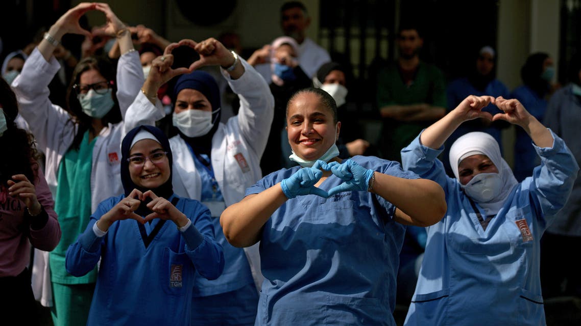 Medical staffers of a Lebanese government hospital show the heart gesture with their hands as a band plays music thanking them for their efforts to support patients during the coronavirus pandemic, in the northern coastal city of Tripoli on April 23, 2020.