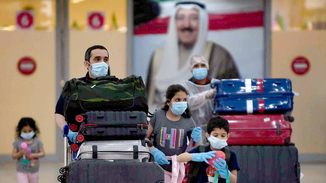 Kuwaiti nationals arrive at the Kuwait International Airport, south of the capital Kuwait City, after a rapatriation plan for citizens stranded abroad was put together by the authorities, on May 3, 2020, during the novel coronavirus pandemic crisis. Behind them hangs a poster of the Emir of Kuwait Sheikh Sabah Al-Ahmad Al-Jaber Al-Sabah. All incoming citizens will be required to undergo home quarantine for 14 consecutive days.