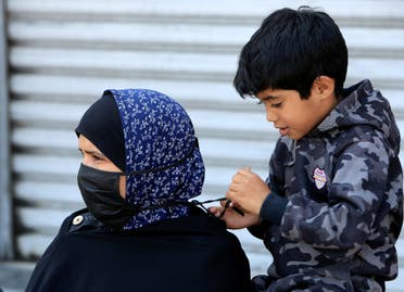 A boy helps his mother to put on a mask, during a countrywide lockdown to combat the spread of coronavirus disease (COVID-19) in Sidon, Lebanon April 28, 2020. (Reuters)