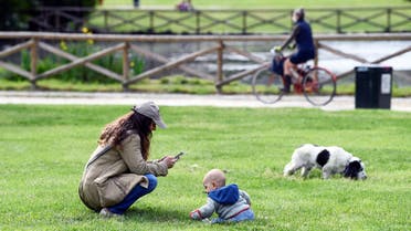 A woman uses her mobile phone at the Sempione park next to a baby, after parks reopen as Italy begins a staged end to a nationwide lockdown due to a spread of the coronavirus disease (COVID-19), in Milan, Italy, May 4, 2020. (Reuters)