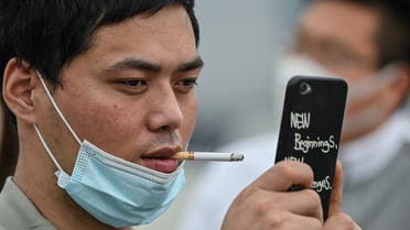 A man smoking a cigarette over a face mask takes a photo at the promenade on the Bund along the Huangpu River during a holiday on May Day, or International Workers' Day, in Shanghai on May 1, 2020. With optimism and a heavy dose of caution, millions of Chinese hit the road or visited newly re-opened tourist sites on May 1 for an extended national holiday in a post-coronavirus confidence test.