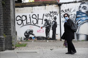 A person wearing a protective face mask walks by streetart in East London following the outbreak of the coronavirus, on May 10, 2020. (Reuters) 