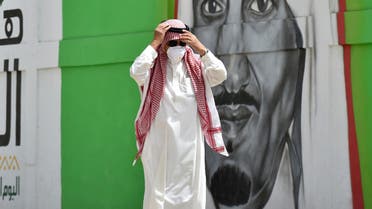 A Saudi man, wearing a protective mask as a precaution against coronavirus, walks past a mural showing the face of King Salman bin Abdulaziz in Riyadh, Saudi Arabia, March 15, 2020. (AFP)