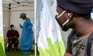 A man looks on through an opening of a tent as a woman watches the heath worker explain the process of collecting a sample for coronavirus testing in Johannesburg, South Africa on May 8, 2020. (AP)