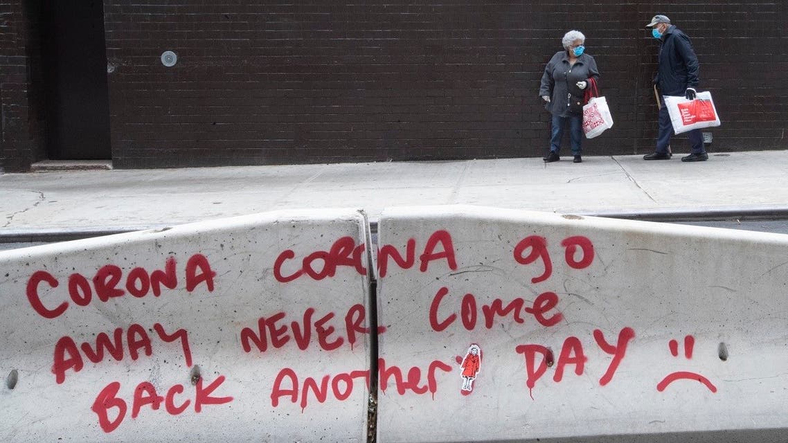 An elderly couple wearing facial masks to protect against the coronavirus walk past graffiti on a street divider calling on the coronavirus to go away, in the Lower East Side of Manhattan on May 11, 2020. (AP)