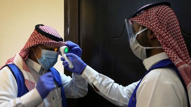 A Saudi volunteer supervisor wearing a protective face mask and gloves checks the temperature of another volunteer before preparing boxes of Iftar meals provided by a charity organisation following the outbreak of the coronavirus disease (COVID-19), during the holy month of Ramadan, in Riyadh. (Reuters)