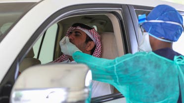 A health worker, wearing personal protective equipment, collects a swab sample from a man at a drive-thru testing service for COVID-19 coronavirus in the Qatari capital Doha. (AFP) 