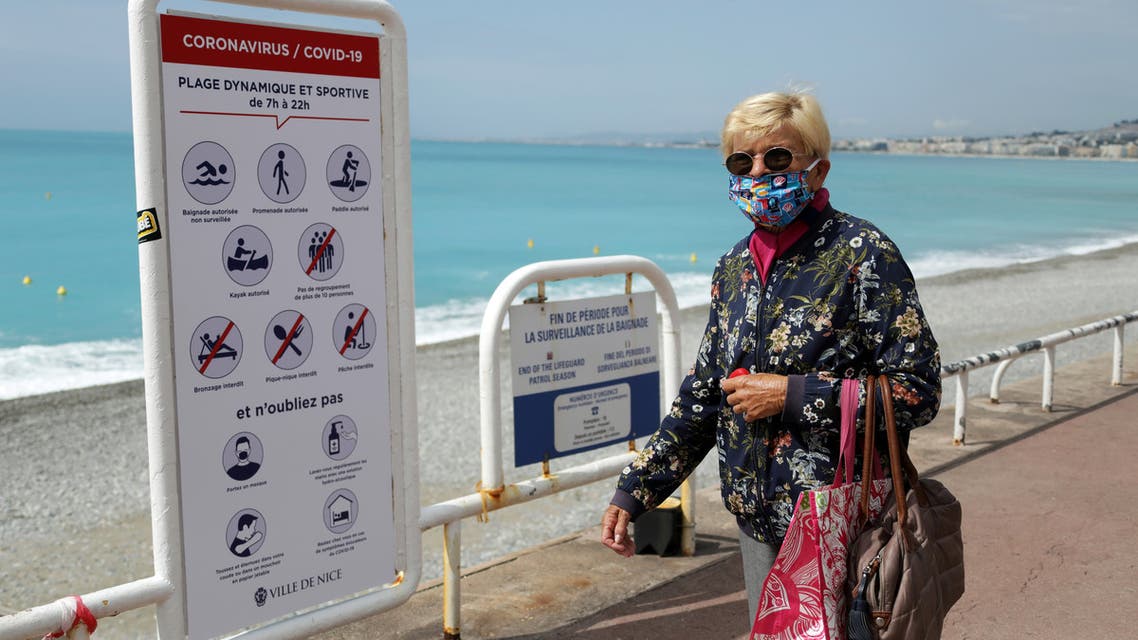 A woman, wearing a protective face mask, walks past a sign reading informations about the safety restrictions at the entrance of a beach on the Promenade des Anglais in Nice on May 16, 2020. (Reuters) 