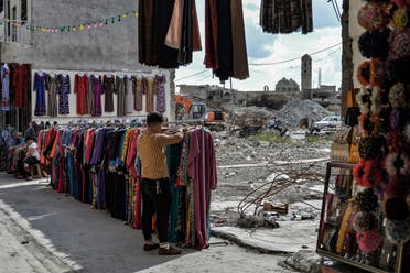 A seller arranges clothes put on display at the Sarj Khaneh market area in the old city of Iraq's northern Mosul, while the damaged Roman Catholic Church of Our Lady of the Hour is seen in the background, on May 3, 2020. (AFP)