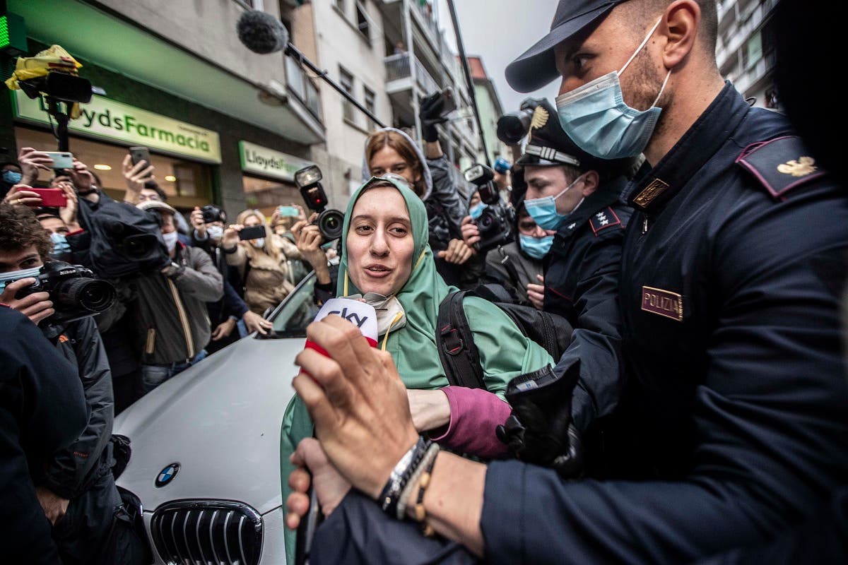 Silvia Romano, escorted by Carabinieri, lowers her face mask for press as she arrives at her home, in Milan, Italy, Monday, May 11, 2020. (AP)