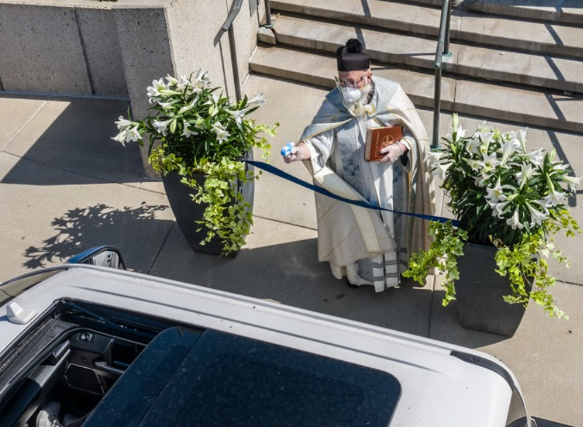 Father Timothy Pelc sprays holy water outside St. Ambrose Church in Grosse Pointe Park, Michigan. (Courtesy: Larry Peplin)