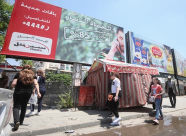 People walk underneath an advertising billboard of Syria's largest mobile operator Syriatel, owned by businessman Rami Makhlouf, in the Syrian capital Damascus on May 11, 2020. (Reuters)