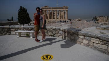 A couple takes selfie picture next to a sticker marking social distance in front of the Parthenon temple on the archeological site of the Acropolis in Athens on May 18, 2020. (AFP)