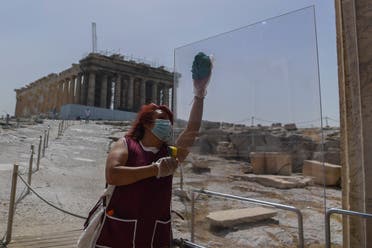 A worker wearing a protective mask cleans a divider made of plexiglass at the entrance of the Acropolis in Athens on May 18, 2020. (AFP)