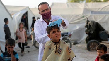 A volunteer hairdresser from ONSUR wearing a face mask and gloves cuts the hair of an internally displaced boy, ahead of the Eid al-Fitr at an IDP camp in Idlib, Syria May 19, 2020. (Reuters)