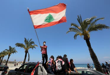 A demonstrator, wearing a mask as a preventive measure against the spread of coronavirus disease waves a national flag during a protest in cars against the growing economic hardship and to mark Labor Day in Tyre, Lebanon May 1, 2020. (Reuters)
