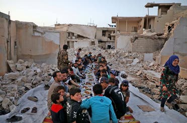 This picture taken on May 12, 2020 in the village of Kafr Nuran in the western countryside of Syria’s northern Aleppo province shows men and children seated together in the midst of ruins before starting the “iftar” fast-breaking meal. (AFP)