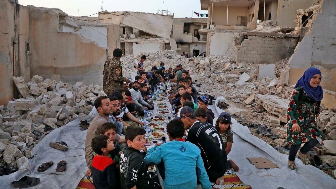 This picture taken on May 12, 2020 in the village of Kafr Nuran in the western countryside of Syria’s northern Aleppo province shows men and children seated together in the midst of ruins before starting the “iftar” fast-breaking meal. (AFP)