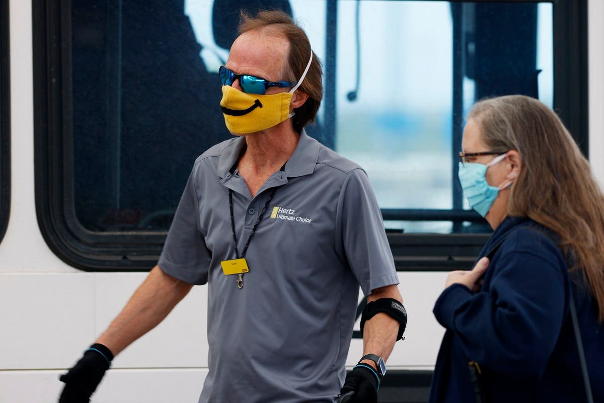 A shuttle driver for Hertz, left, wears a face mask with a built-in smile as he helps a traveler board the bus outside the main terminal at Denver International Airport as easing of restrictions of the new coronavirus start, Wednesday, May 13, 2020. (Reuters)
