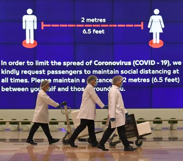 Employees at Dubai International Airport, walk past a poster reminding passengers to keep a safe distance from each other, after the resumption of scheduled operations by the Emirati carrier Emirates airline, amid the ongoing novel coronavirus pandemic crisis, on May 22, 2020. (AFP)