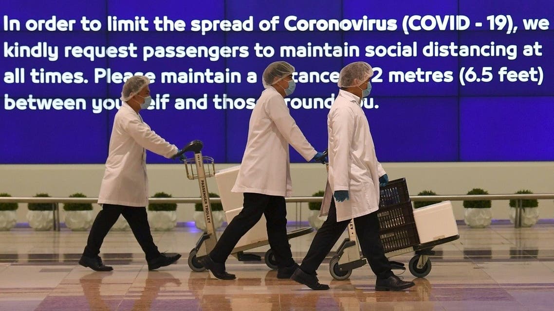 Employees at Dubai International Airport, walk past a poster reminding passengers to keep a safe distance from each other, after the resumption of scheduled operations by the Emirati carrier Emirates airline, amid the ongoing novel coronavirus pandemic crisis, on May 22, 2020. (AFP)