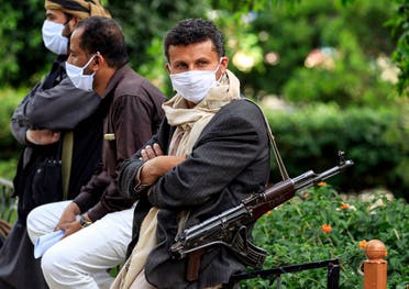 A fighter loyal to Yemen's Houthi rebels acting as security, looks on while wearing a face mask and latex gloves and slinging a Kalashnikov assault rifle as volunteers part of a community-led initiative to prevent the spread of COVID-19 coronavirus disease gather in Yemen's capital Sanaa on May 14, 2020. (AFP)