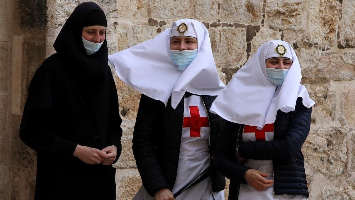 Christian nuns wearing face masks stand outside the shut doors of the Church of the Holy Sepulchre in Jerusalem’s Old City on May 24, 2020, closed due to the coronavirus pandemic lockdown. (AFP)