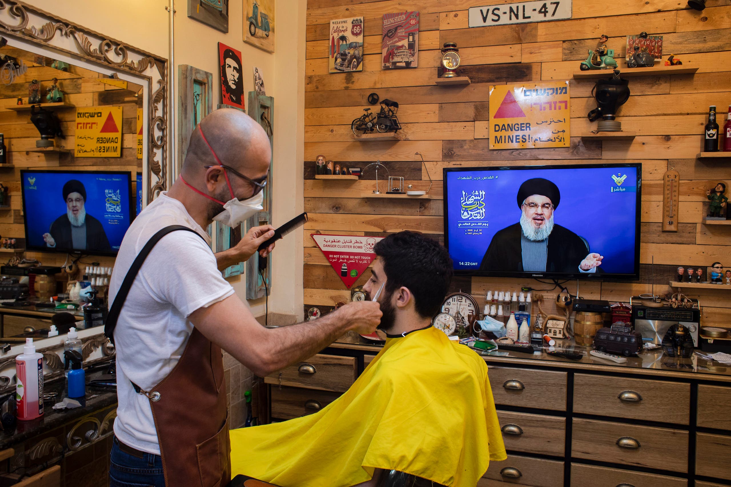 A barber wearing a mask listens to a speech by Hezbollah leader Hassan Nasrallah in the southern suburb of Beirut, Lebanon, Friday, May 22, 2020. (AP)