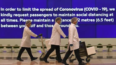 Employees at Dubai International Airport, walk past a poster reminding passengers to keep a safe distance from each other, after the resumption of scheduled operations by the Emirati carrier Emirates airline, amid the ongoing novel coronavirus pandemic crisis, on May 22, 2020.