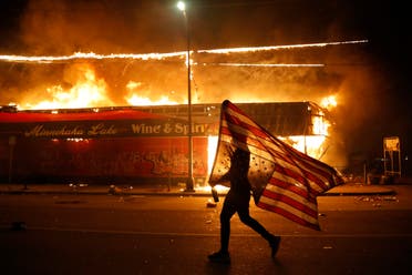 A protester carries a U.S. flag upside down, a sign of distress, next to a burning building Thursday, May 28, 2020, in Minneapolis. Protests over the death of George Floyd, a black man who died in police custody Monday, broke out in Minneapolis for a third straight night. (AP)