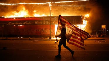 A protester carries the carries a U.S. flag upside, a sign of distress, next to a burning building Thursday, May 28, 2020, in Minneapolis. (AP)