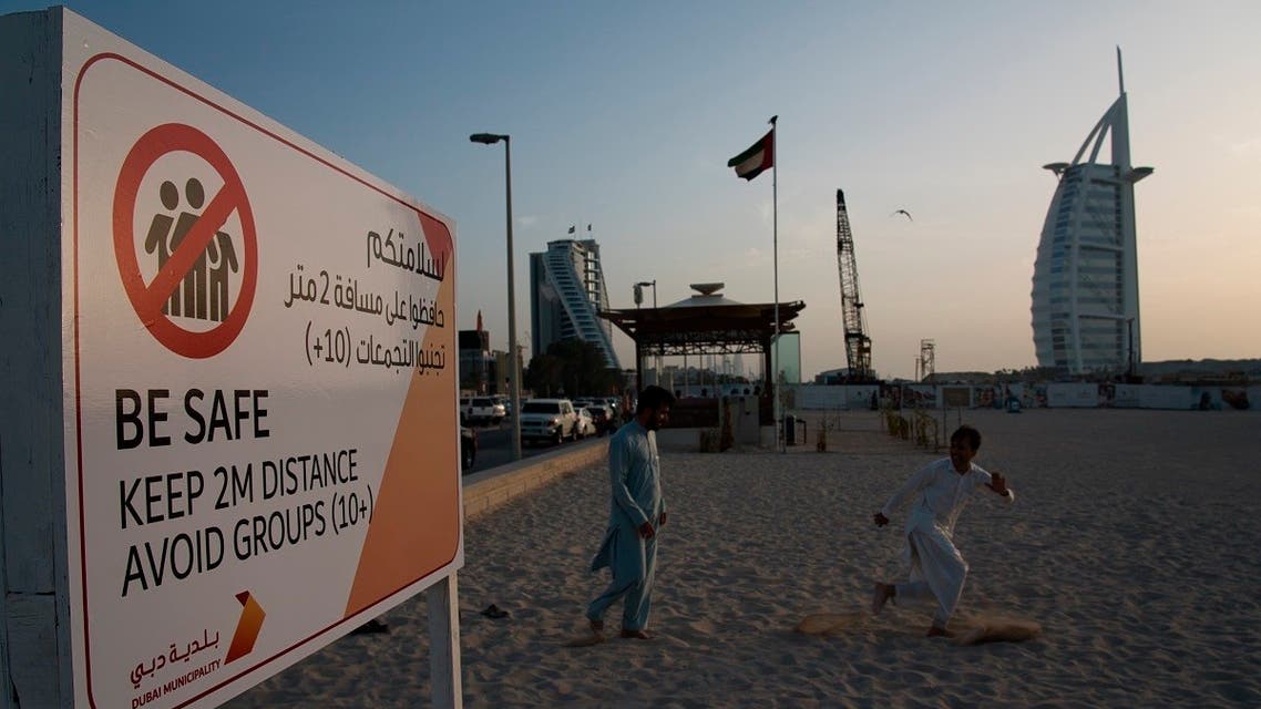 two laborers play tag near a sign warning people to maintain a distance from each other over the outbreak of the new coronavirus in front of the sail-shaped Burj Al Arab luxury hotel in Dubai, United Arab Emirates. (AP)