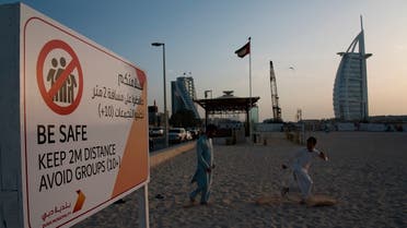 two laborers play tag near a sign warning people to maintain a distance from each other over the outbreak of the new coronavirus in front of the sail-shaped Burj Al Arab luxury hotel in Dubai, United Arab Emirates. (AP)