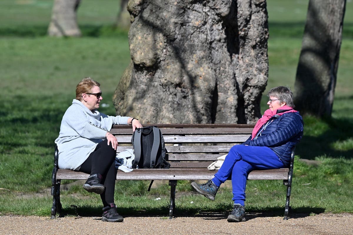people sit at either end of a park bench as they talk in Clapham Common in south London on March 24, 2020. (AFP)